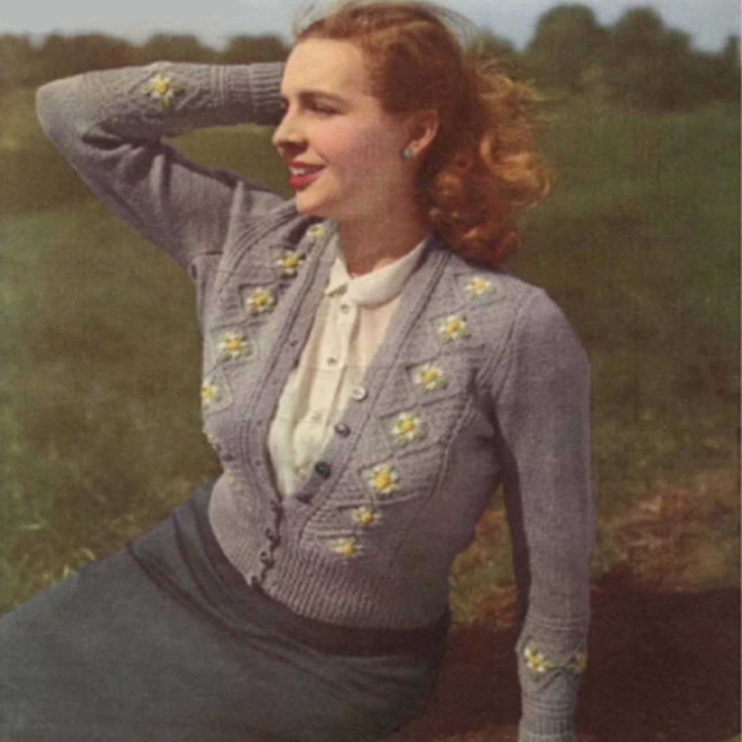 Woman in an embroidered cardigan sitting in a field