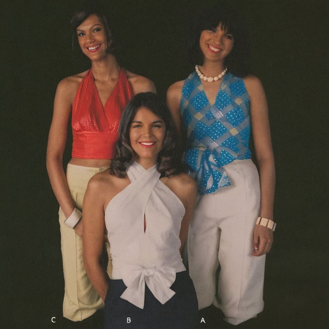 Three women posing together against a black background, wearing colorful tops and pants.