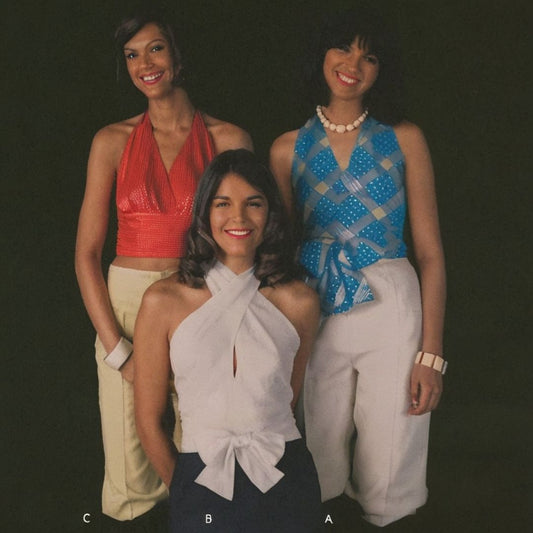 Three women posing together against a black background, wearing colorful tops and pants.