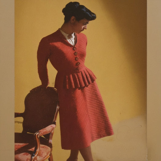 Woman in a red dress standing next to a chair against a yellow wall