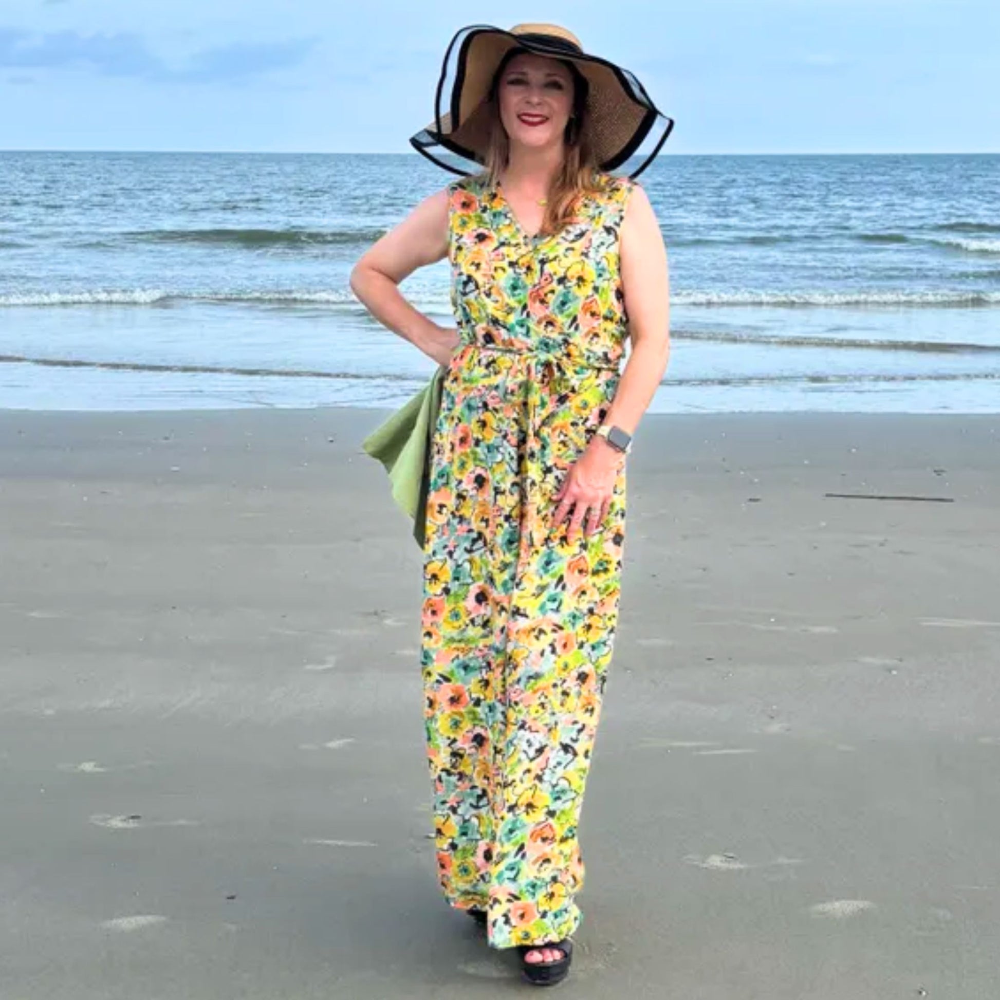 Woman in a floral dress and sun hat standing on a beach.