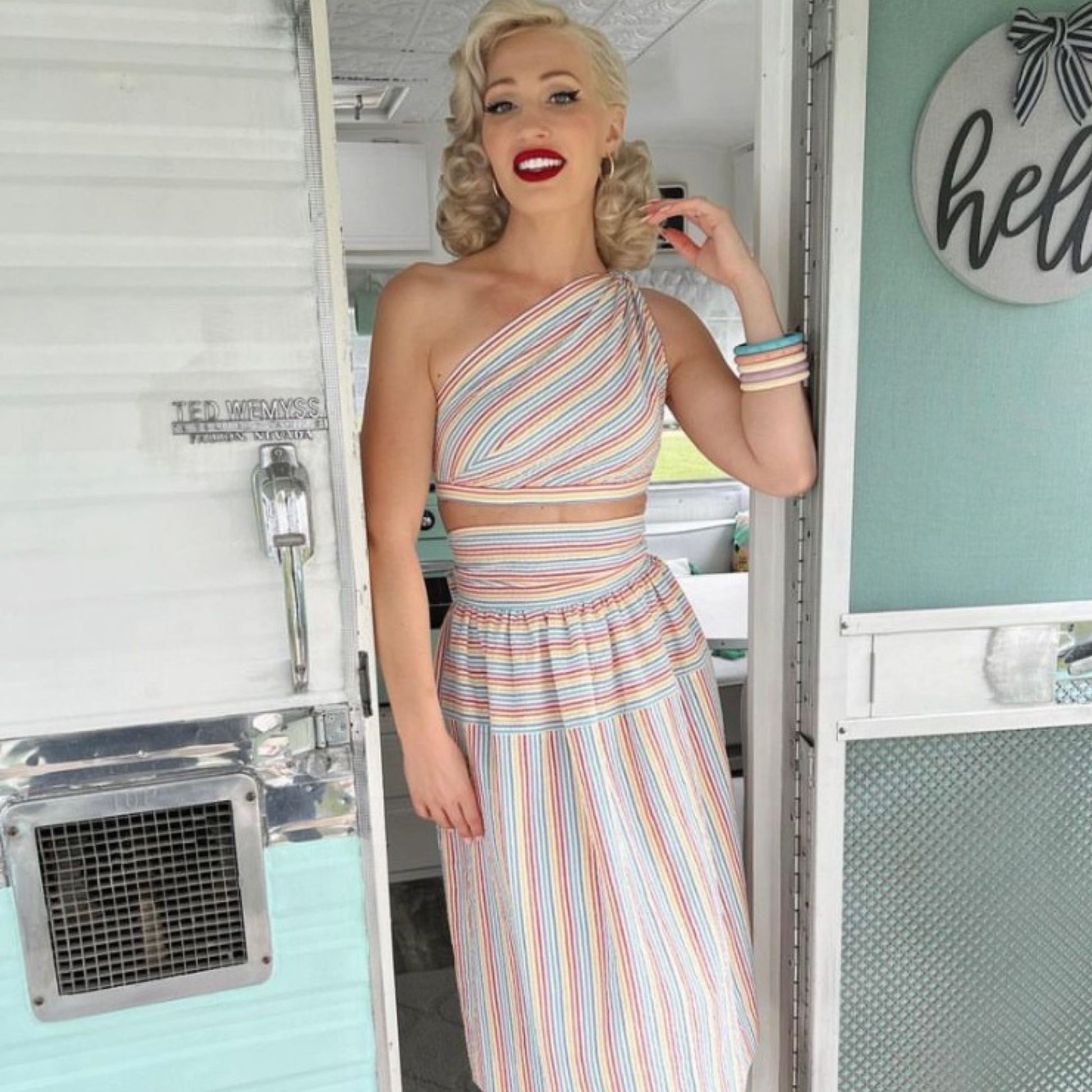 Woman in a striped dress standing in front of a vintage trailer.