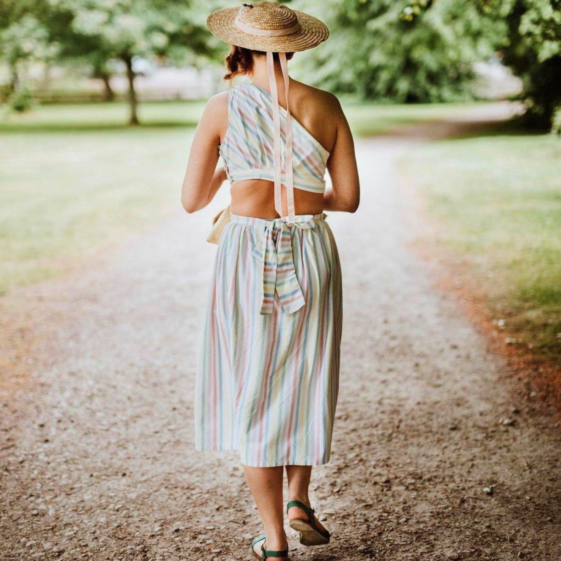 Woman in a colorful dress and straw hat walking on a dirt path in a park.
