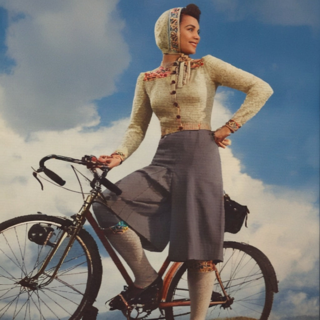 Woman in vintage attire standing next to a bicycle against a blue sky with clouds