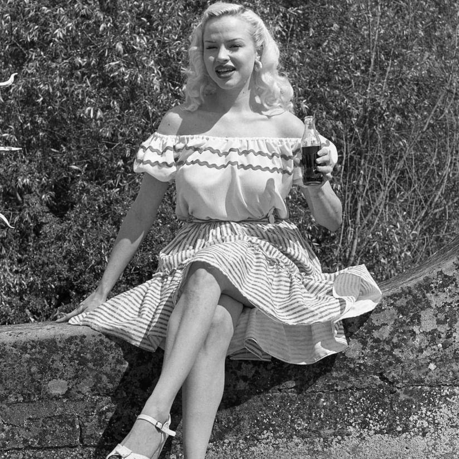 Blonde haired girl sat on a wall wearing a 1950s gypsy top